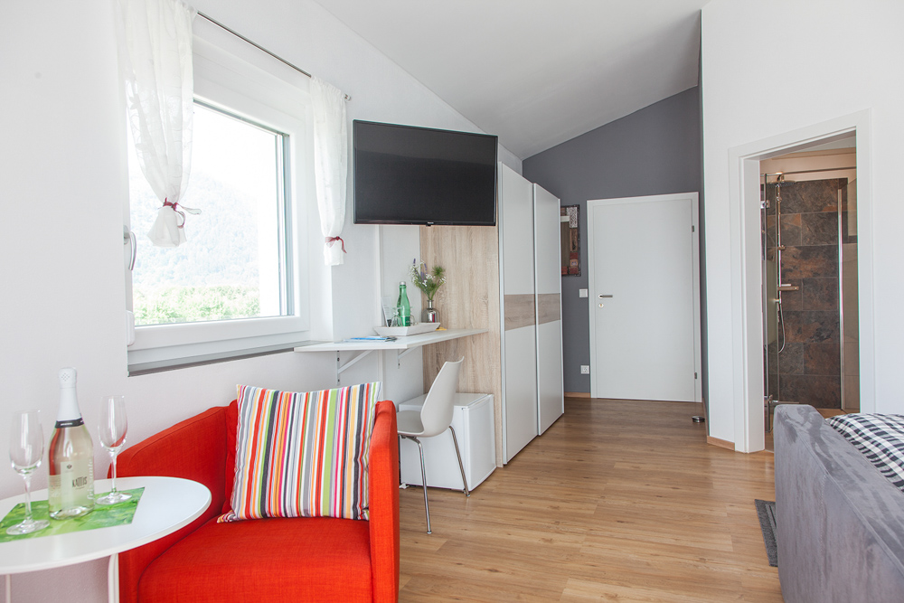 „Hahns Herberge“ – Schlafzimmer mit Blick zu Tür Innenansicht; Einrichtung in rot und grau gehalten, funktionale Einrichtung.